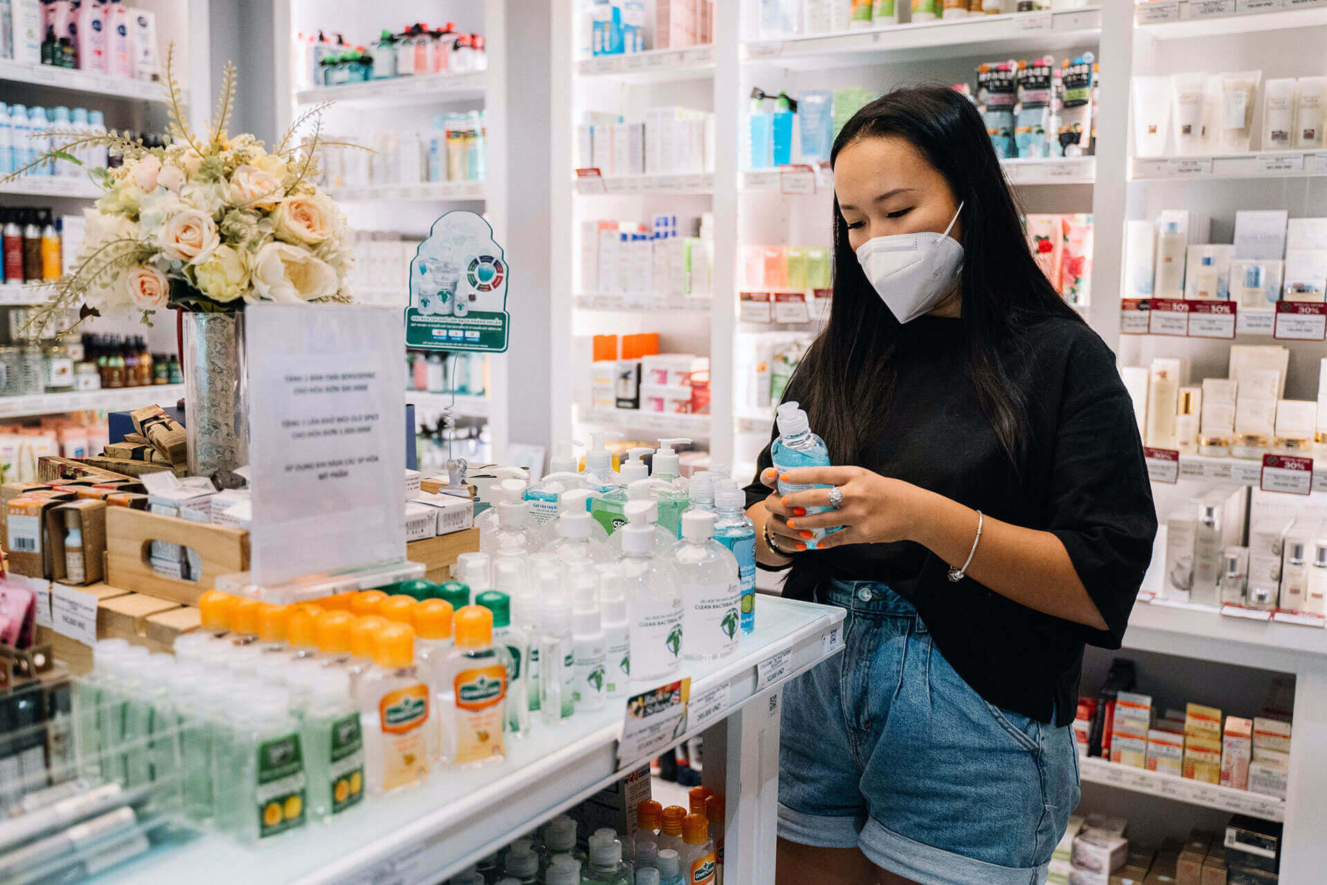 woman wearing mask and holding a bottle in her hand inside a pharmacy